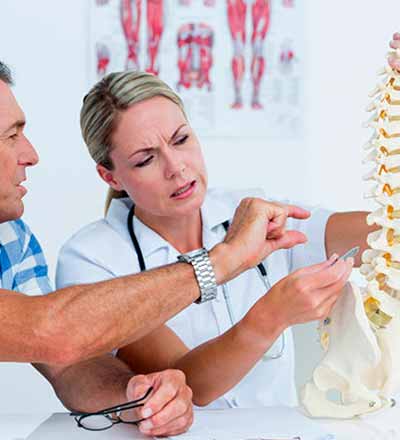 Un hombre y su médica hablando delante de un modelo de columna vertebral - Tratamientos de fisioterapia - Fisioterapia neurológica
